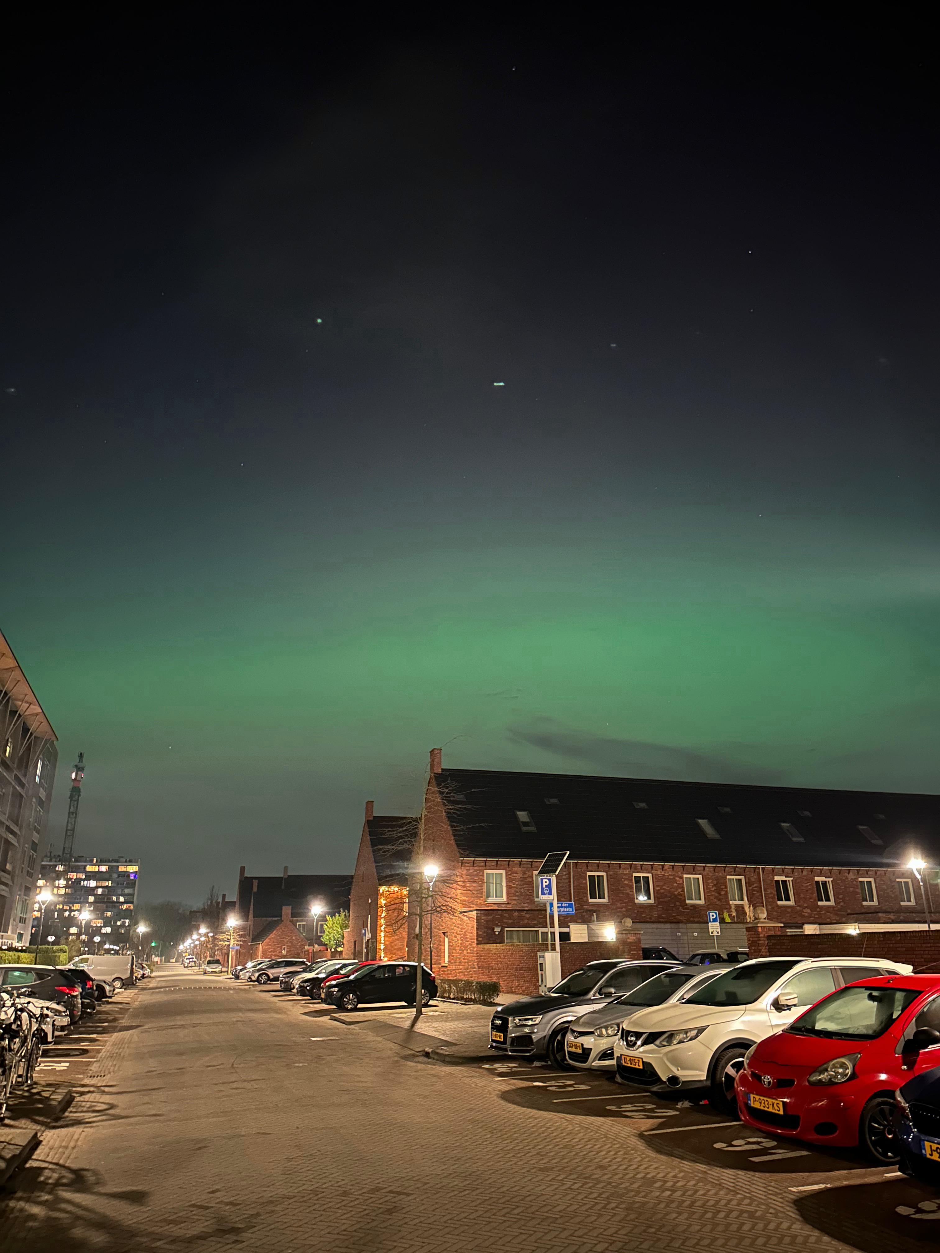 Green aurora above brick houses and parked cars at night