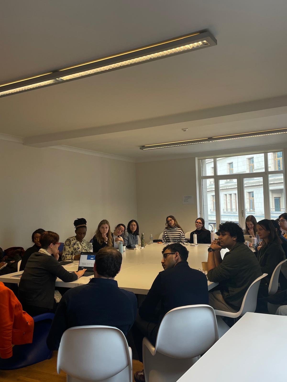 Group seated around a white table in a bright seminar room with large windows